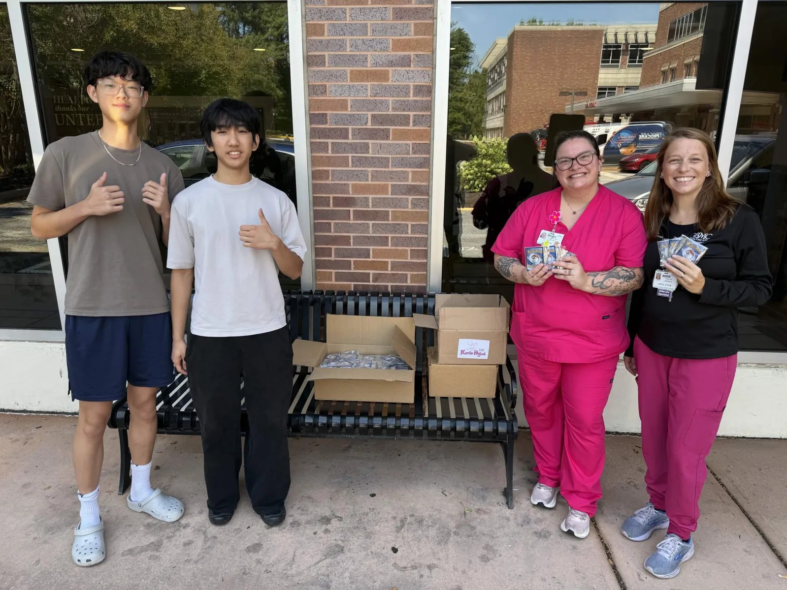 Four people beside boxes of Pokémon card packs outside a building.