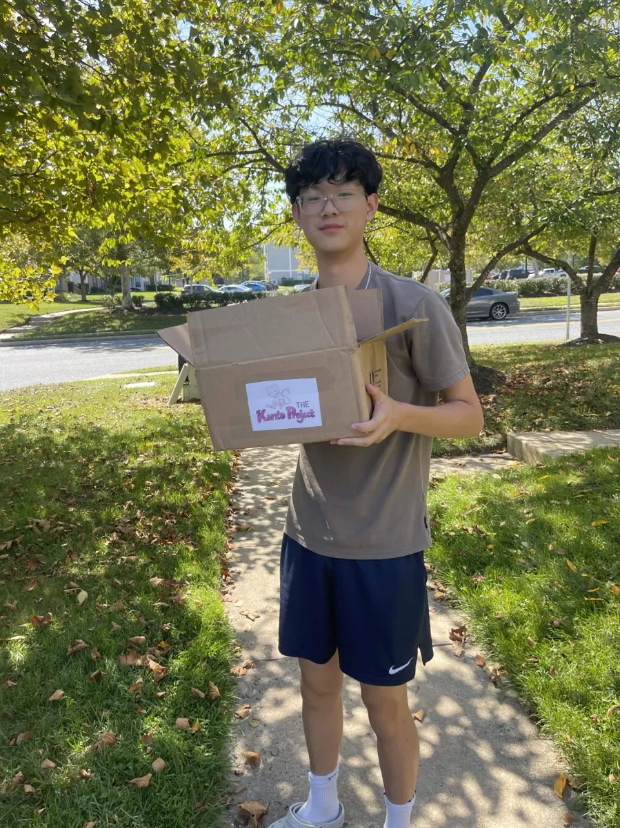 A person carrying a box with The Kanto Project logo outdoors.