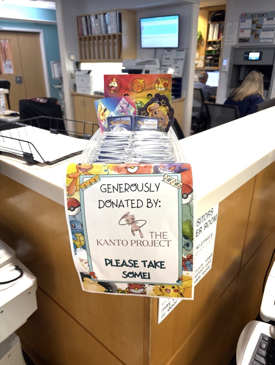 Pokémon card packs at a reception desk with a sign crediting The Kanto Project.